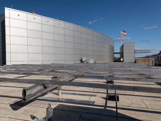 Aluminum racking frame under construction on the roof of 20 M Street, beside a curved metal penthouse wall
