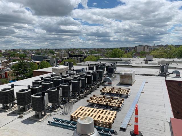 Roof of Randolph Towers with rows of condenser units and pallets of racking material before installation