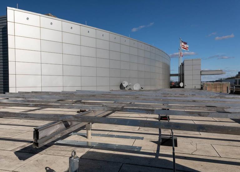Aluminum racking frame under construction on the roof of 20 M Street, beside a curved metal penthouse wall