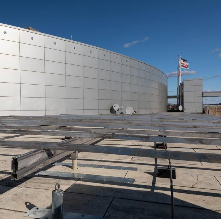 Aluminum racking frame under construction on the roof of 20 M Street, beside a curved metal penthouse wall